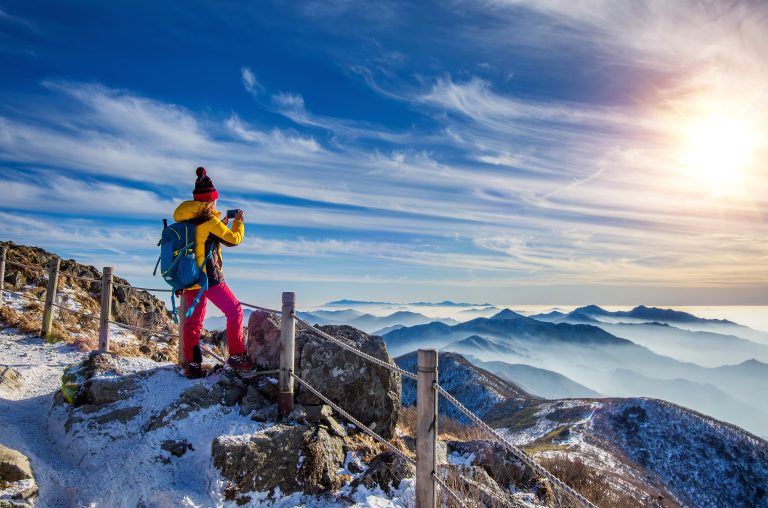 young woman hiker taking photo with smartphone on mountains peak